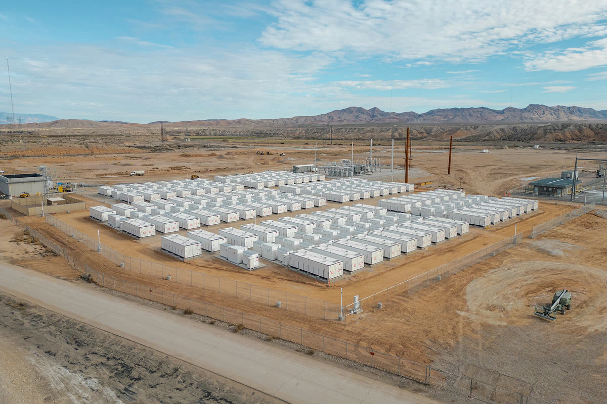 Aerial view of rows of white battery enclosures inside a fenced desert site, with the site substation at the edge