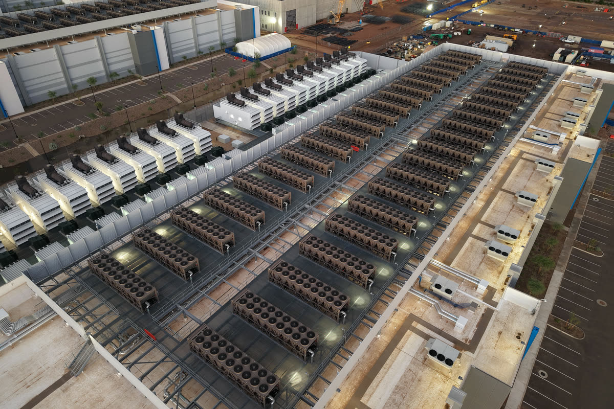 Aerial view at dusk of a data centre roof covered with rows of chillers and cooling units, with generator enclosures alongside