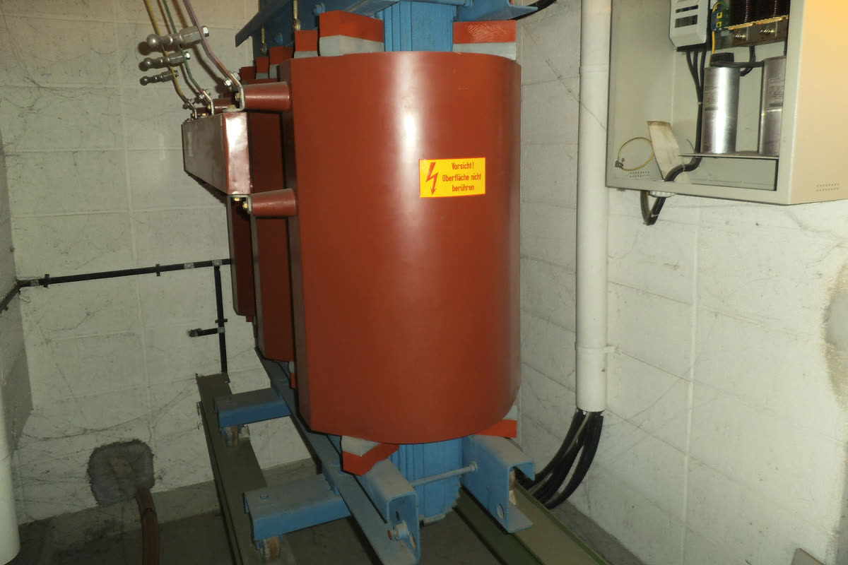 Cast resin dry type transformer with red resin encapsulated coils on a blue frame, installed indoors with cables entering from above