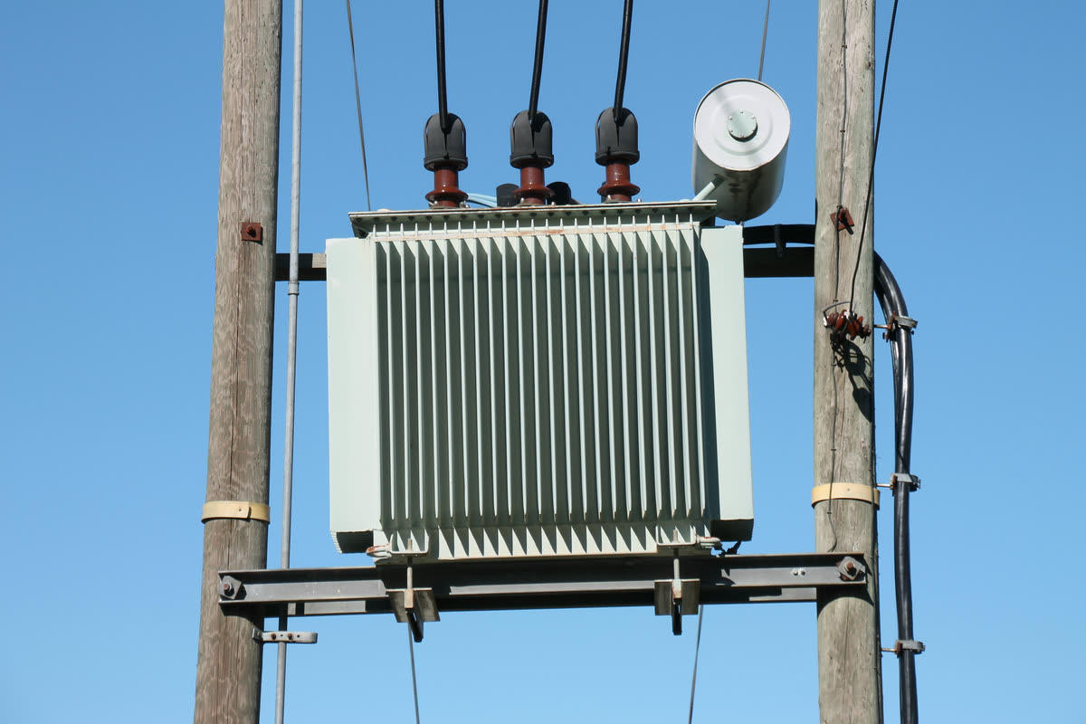 Three phase oil immersed distribution transformer with corrugated cooling fins and three medium voltage bushings, mounted on a two pole structure